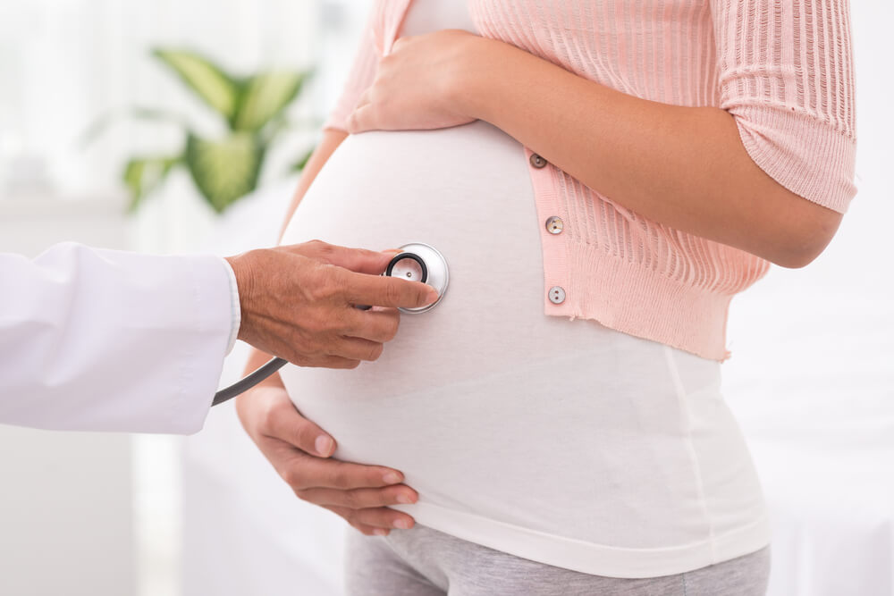 Médico examinando a una mujer embarazada con un estetoscopio