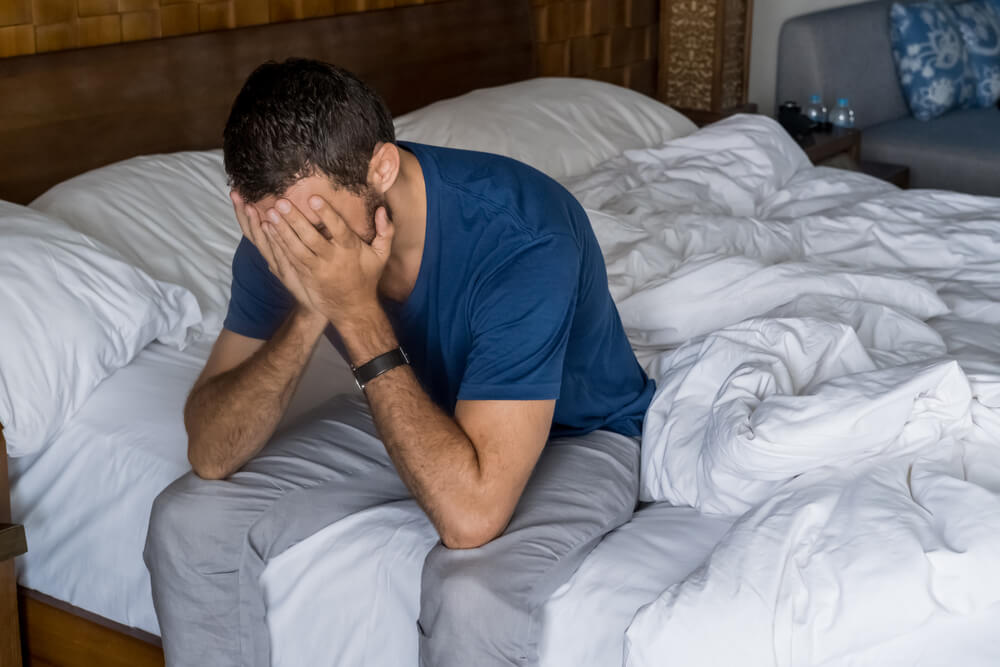 Hombre sentado en la cama cubriendo la cara con las manos y llorando