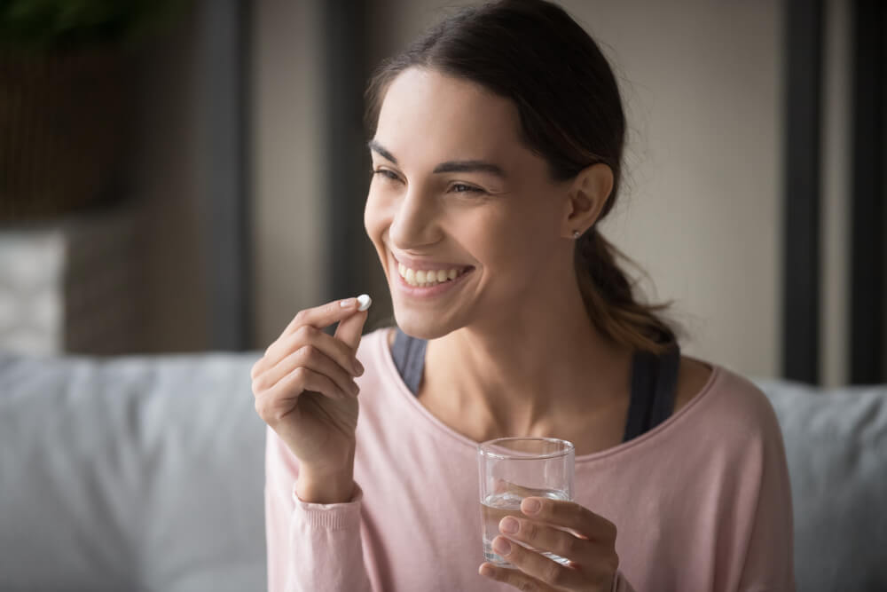 Mujer joven sonriendo con una pastilla en la mano.