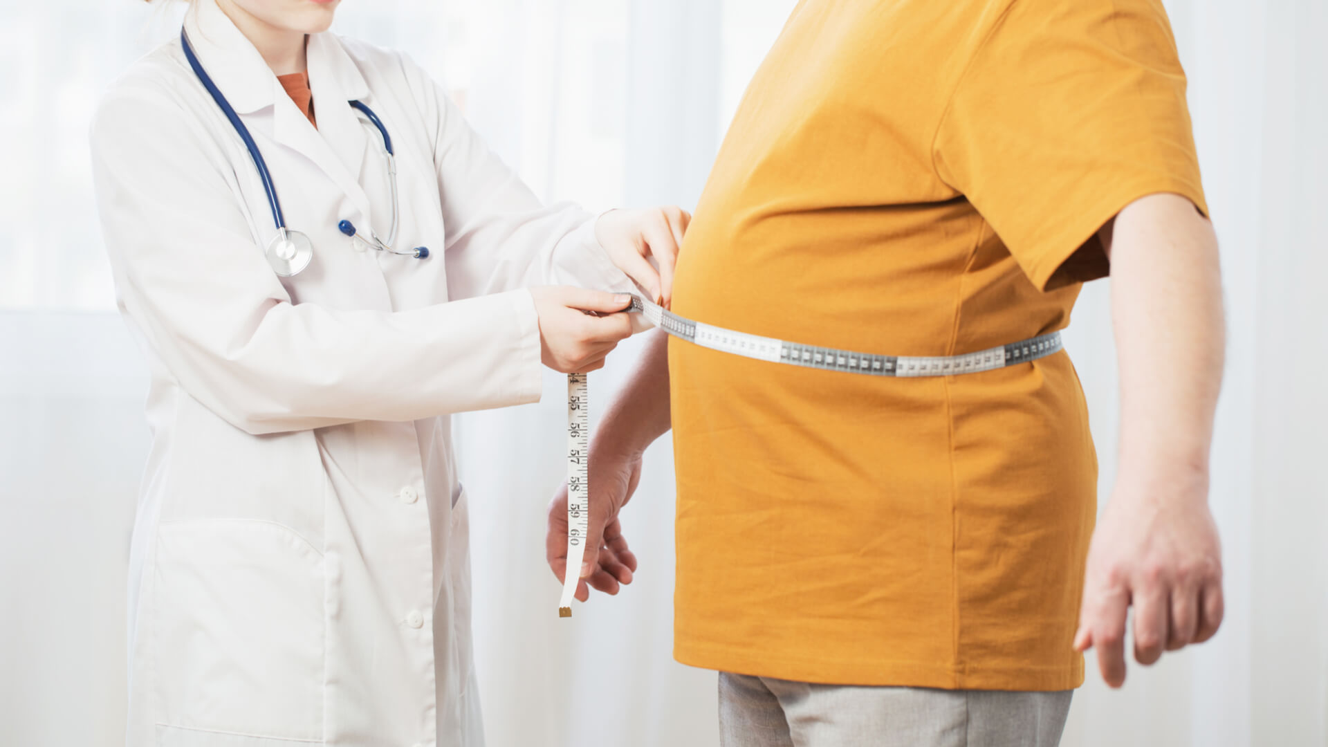 Doctor mide la cintura de un hombre con sobrepeso.