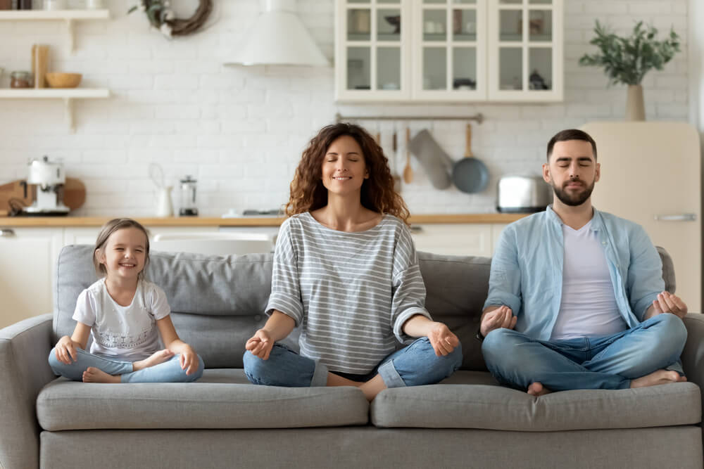 Pareja joven con su hija pequeña meditando en el sofá.